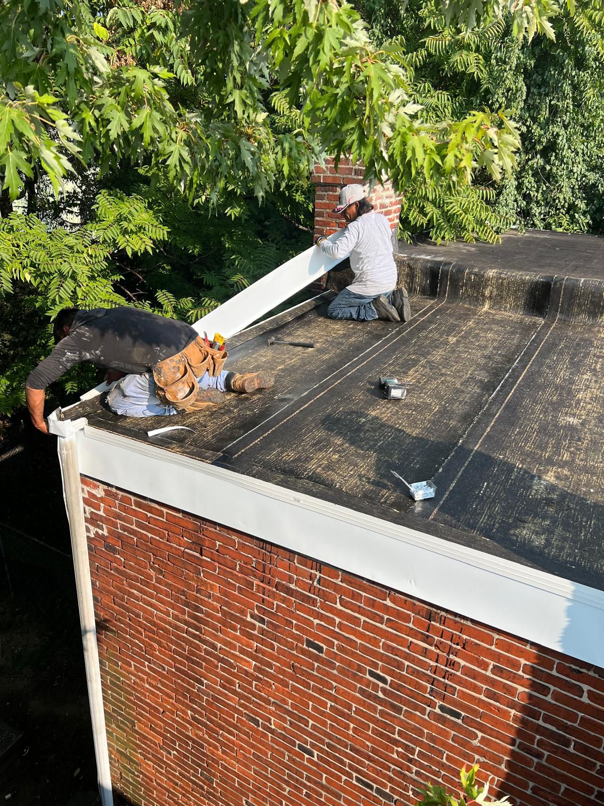 Roofing crew repairing a flat low-slope roof along the parapet wall
