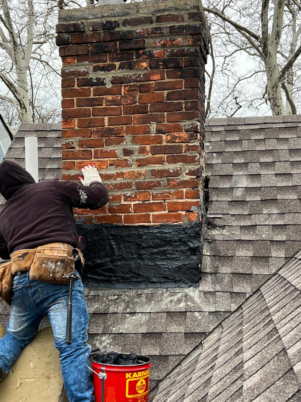 Chimney contractor repairing a brick chimney with new step flashing and base waterproofing on a Northern NJ home