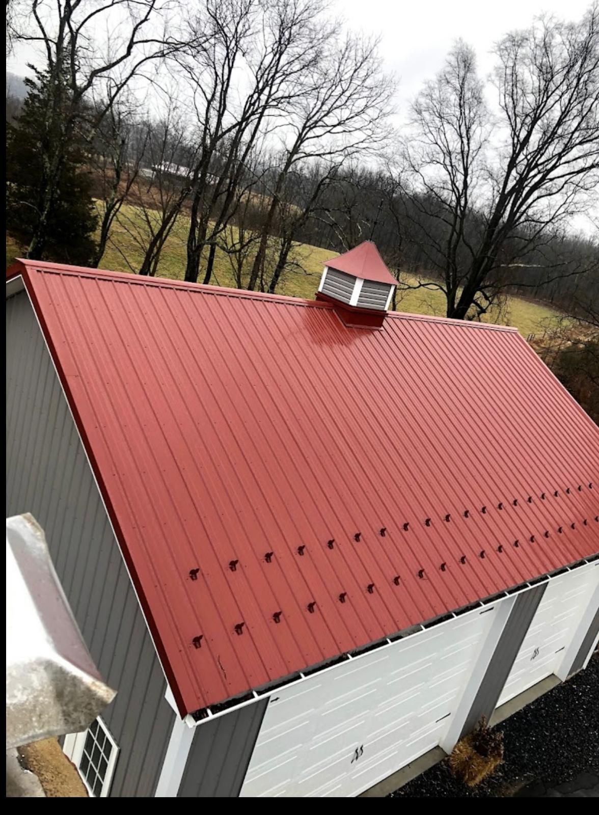 Red standing-seam metal roof installed on a barn-style outbuilding
