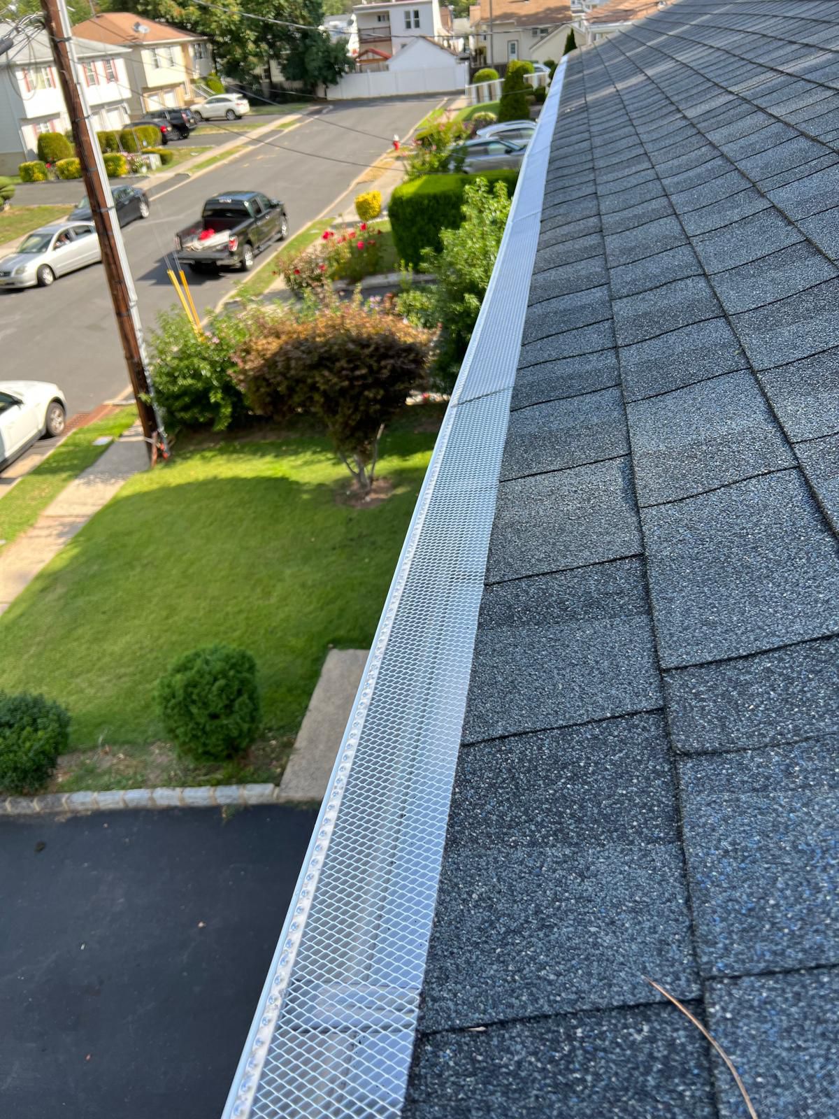 Long run of seamless aluminum gutter with stainless mesh leaf guard alongside an asphalt shingle roof in Northern NJ
