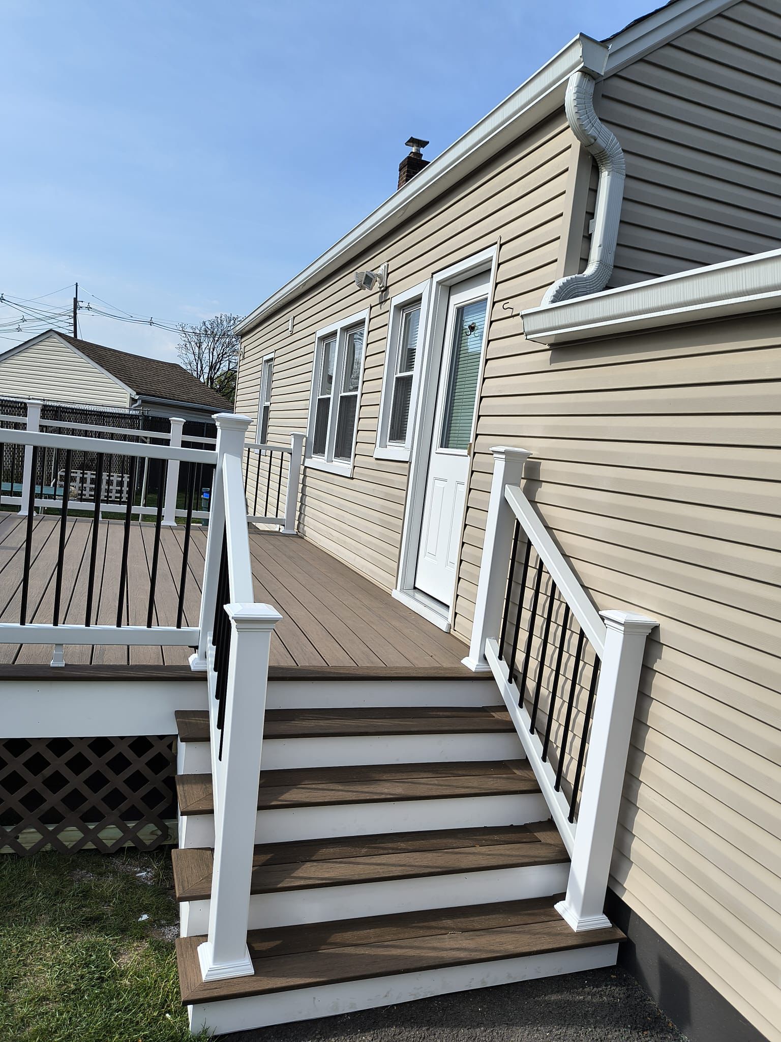 Composite deck stairs leading up to a side entry with white railings on tan siding