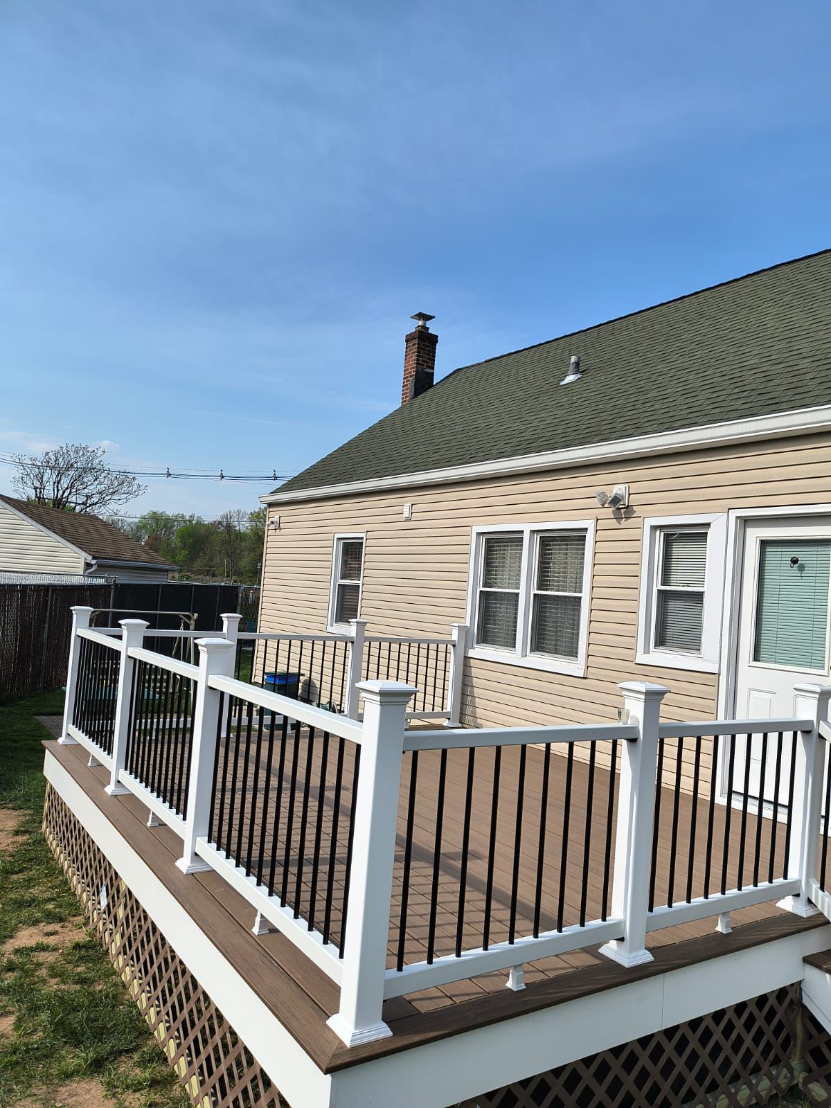 Wide composite deck with white railings overlooking a fenced backyard in Northern NJ — built by Randy's Roofing Construction
