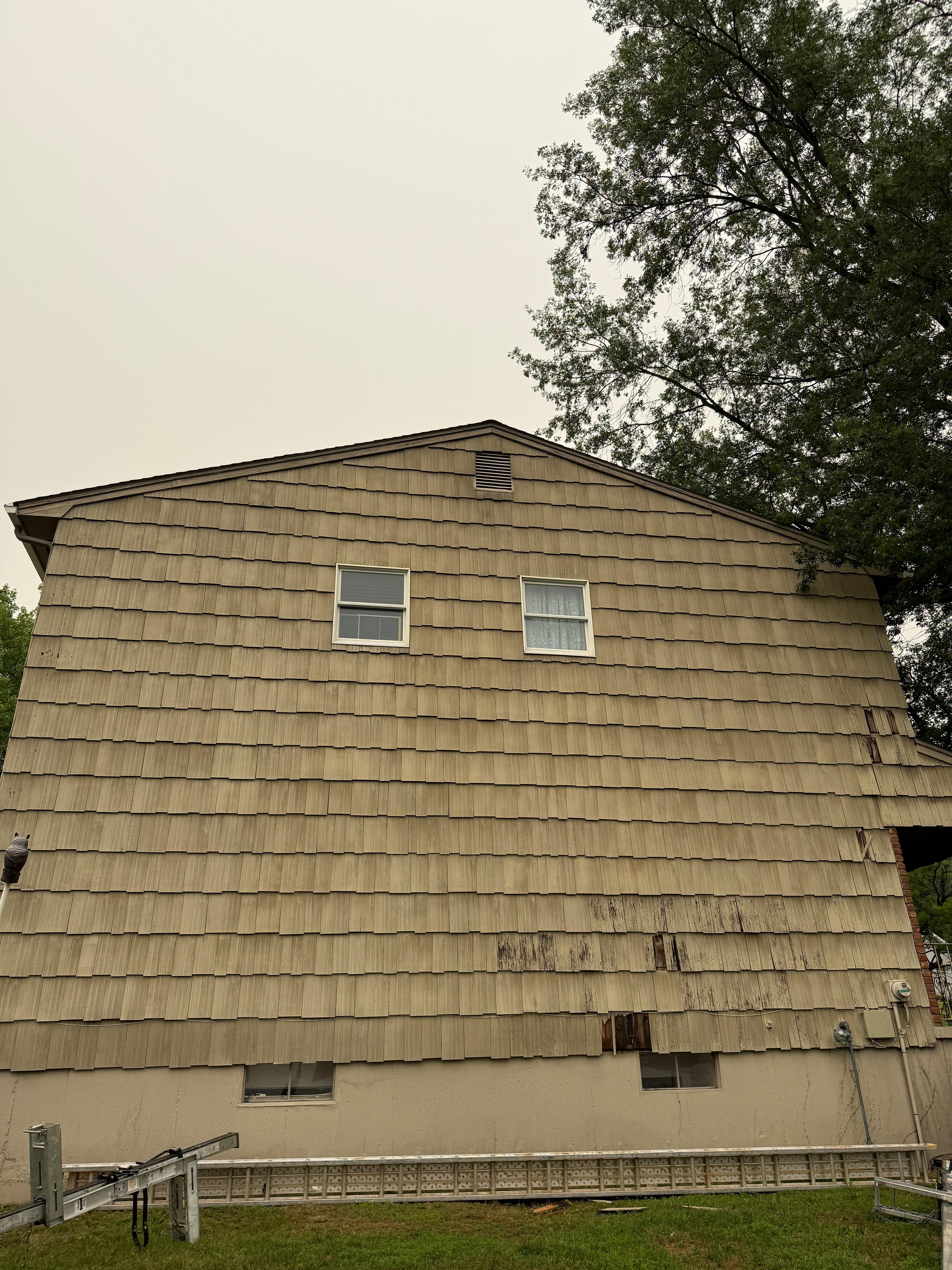 Gable wall of the home before work begins, with a ladder staged along the foundation