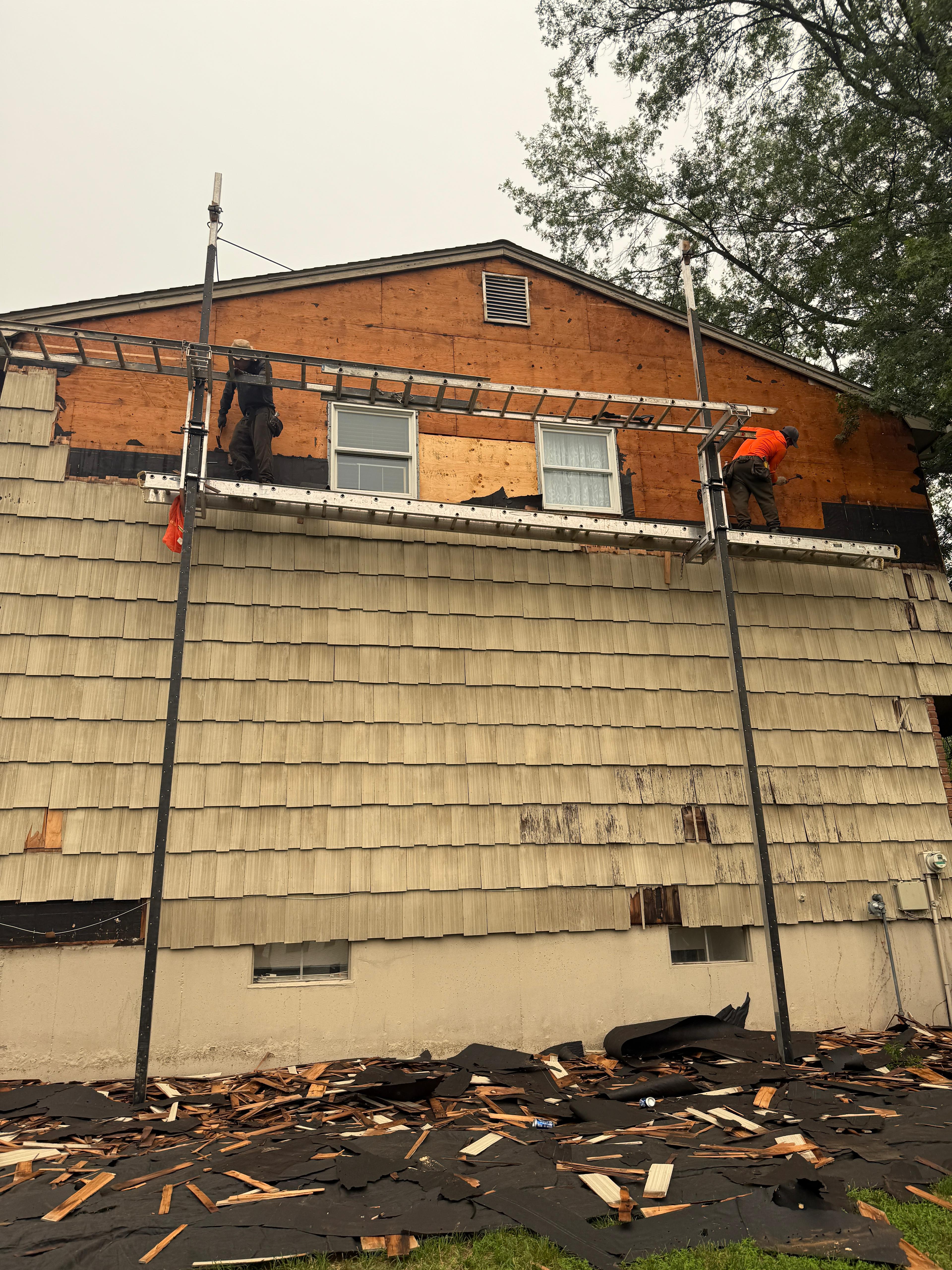 Two installers on pump-jack scaffolding stripping shake siding down to bare plywood sheathing
