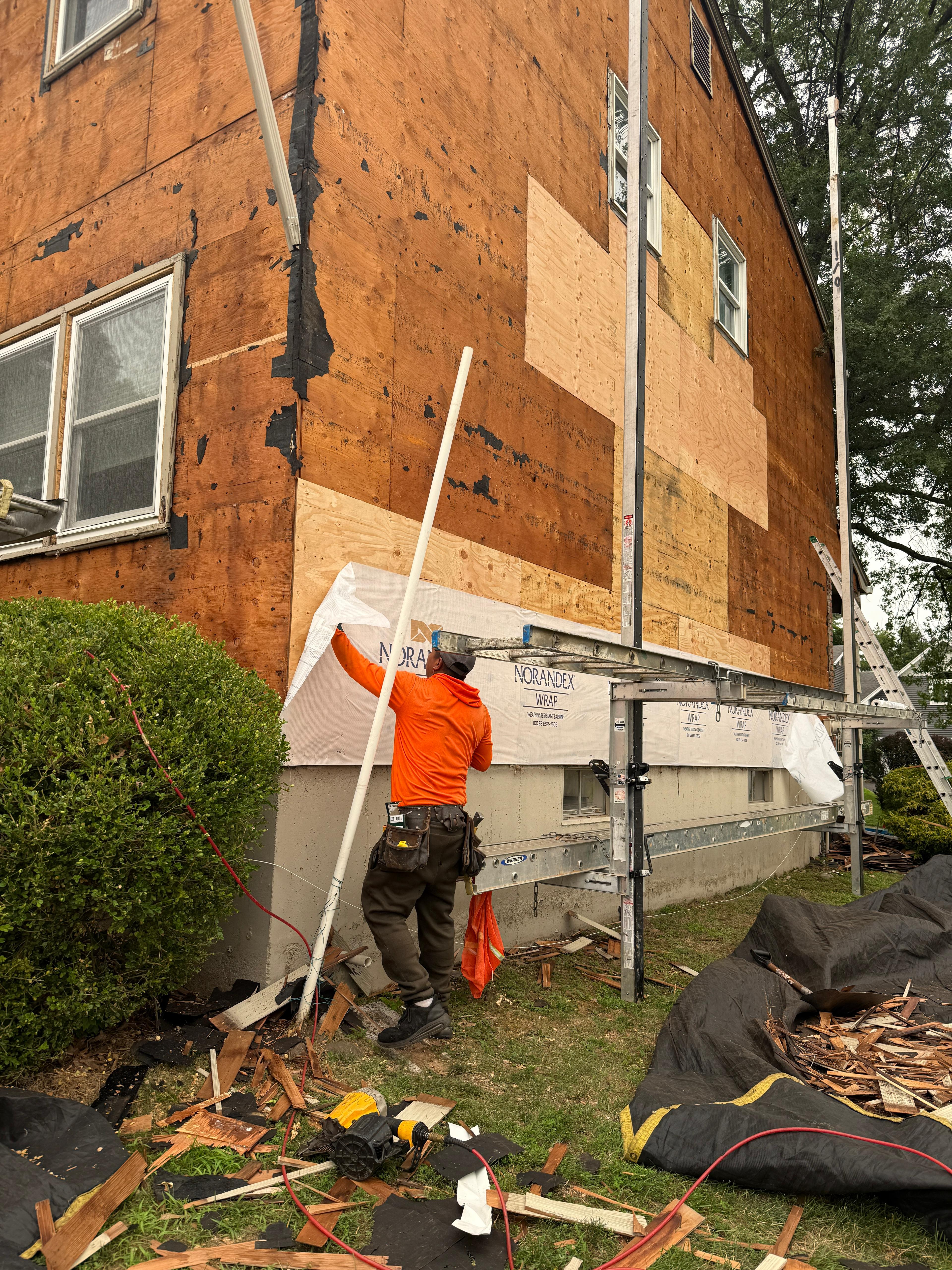 Installer applying Norandex housewrap over freshly replaced plywood sheathing patches