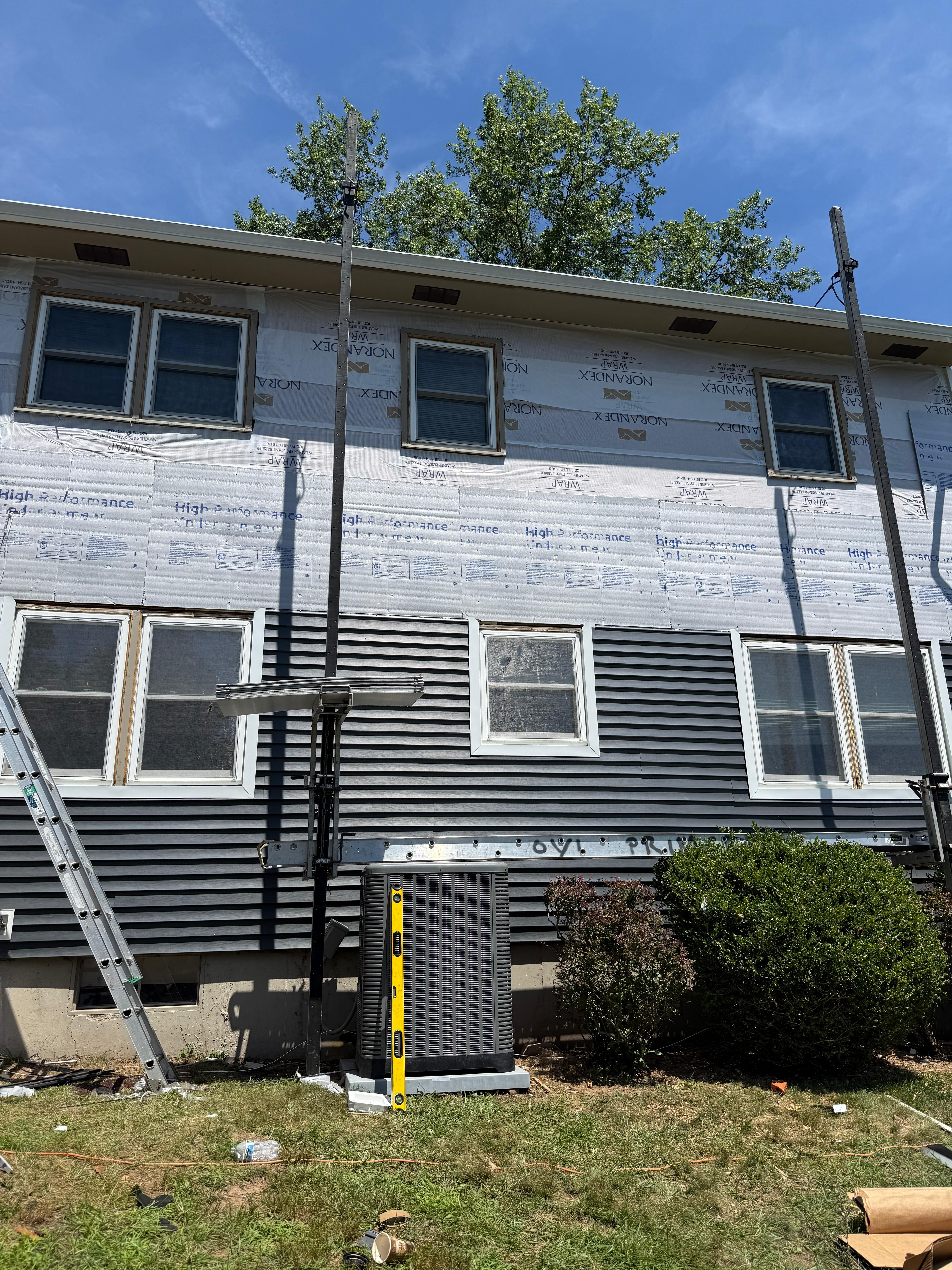 Navy vinyl siding being installed bottom-up over white housewrap and underlayment board