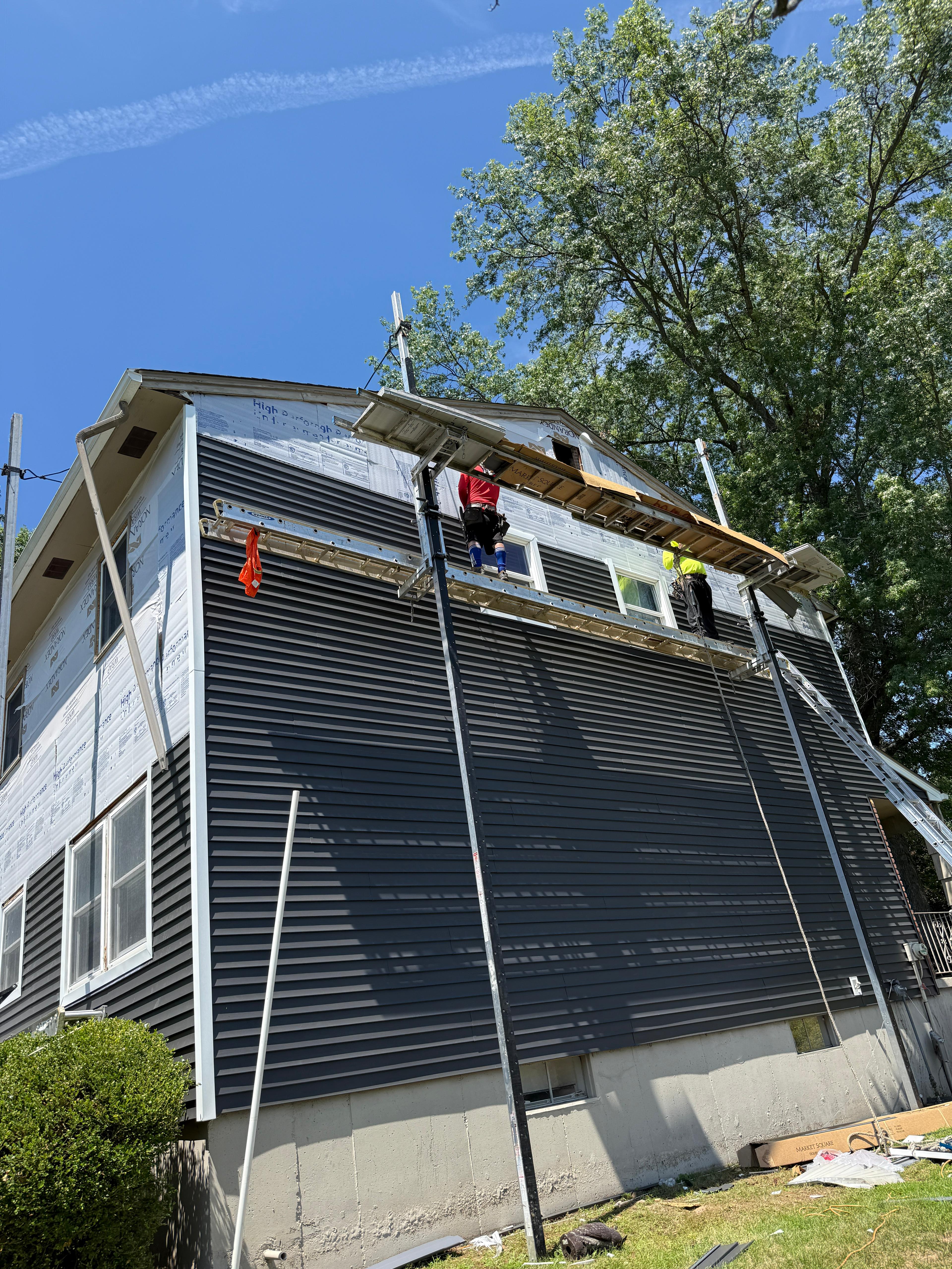 Installers working the upper courses of navy siding from scaffolding