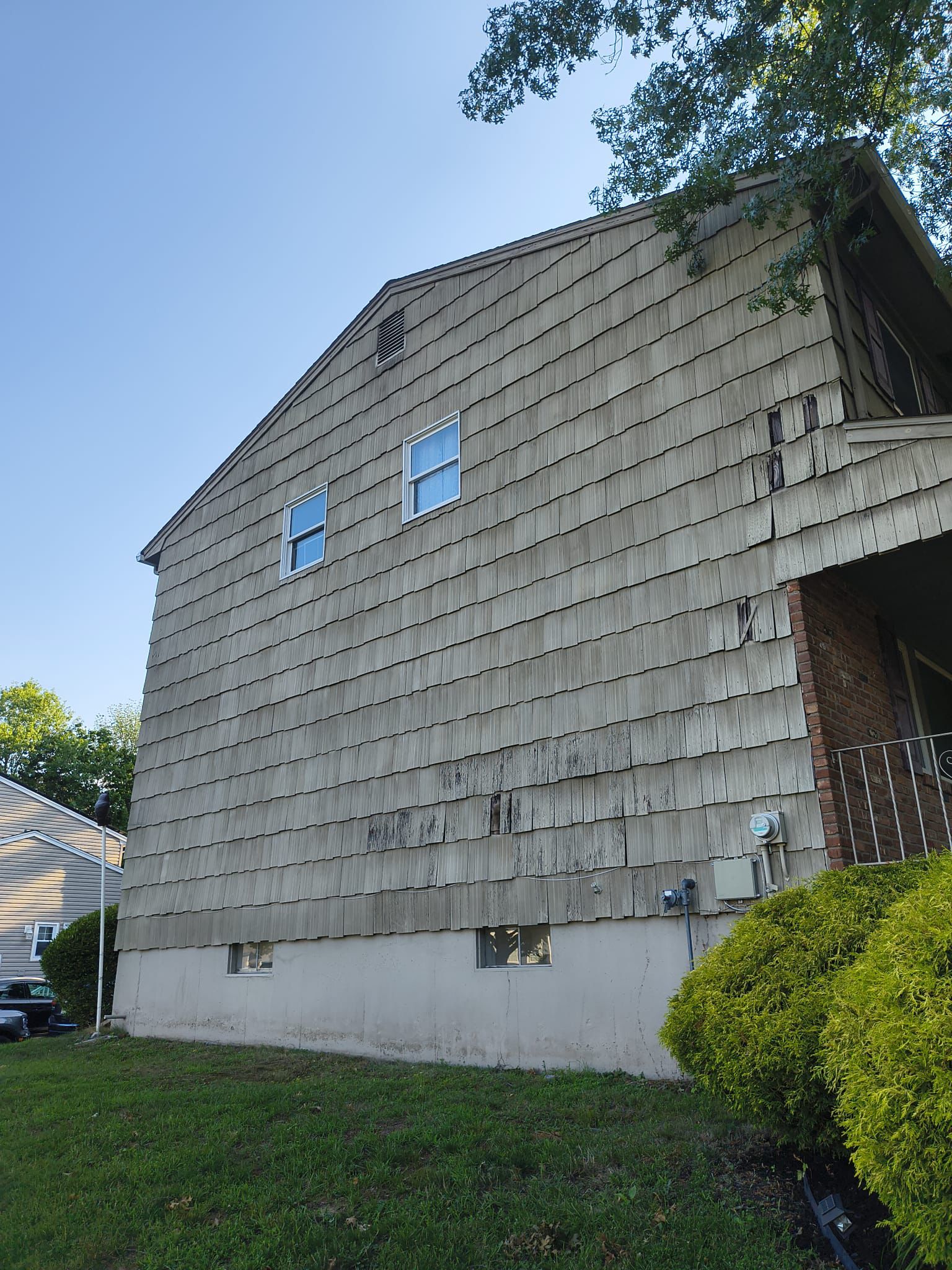 Weathered cedar shake siding with split and missing courses above the foundation line