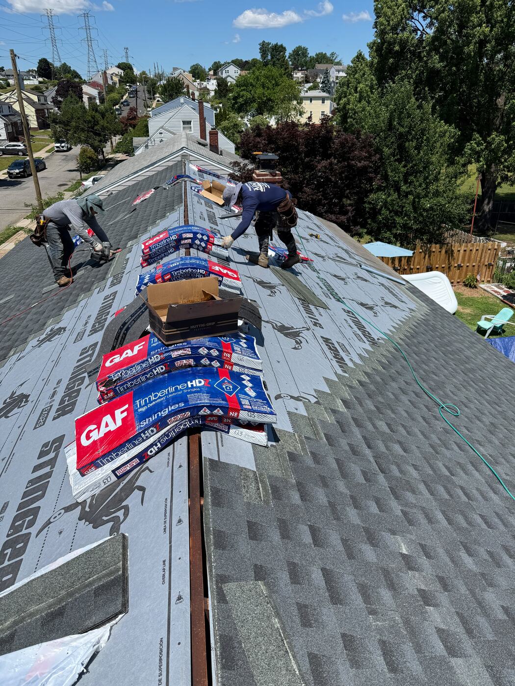 Two roofers nailing GAF Timberline HDZ shingles while working down the slope from the ridge