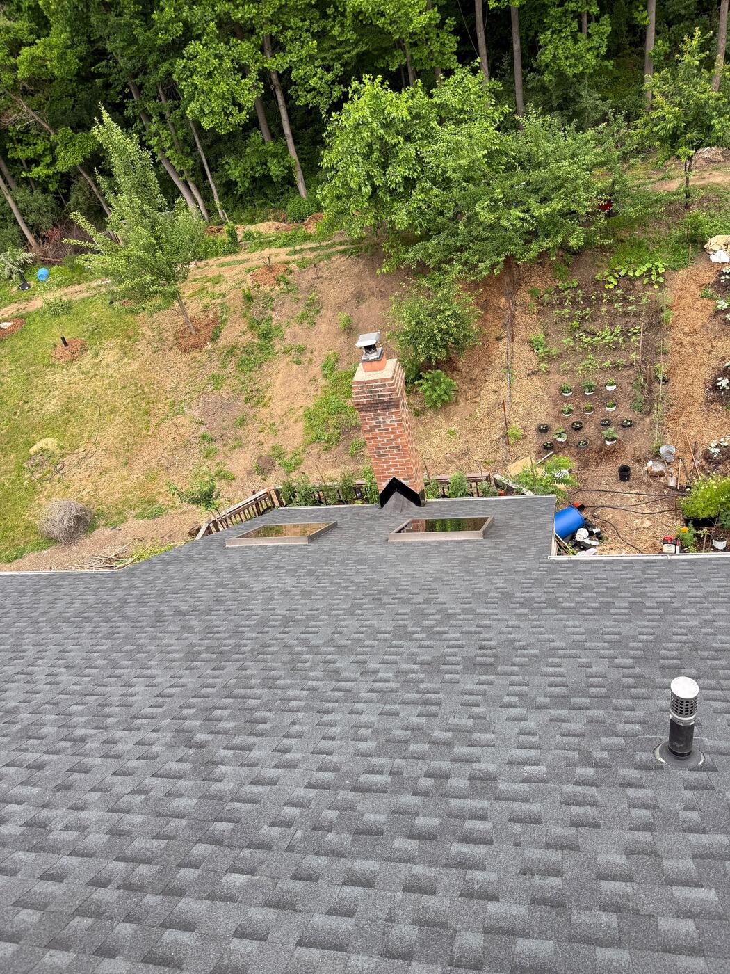 Brick chimney and two skylights set into the finished shingle roof above a hillside garden