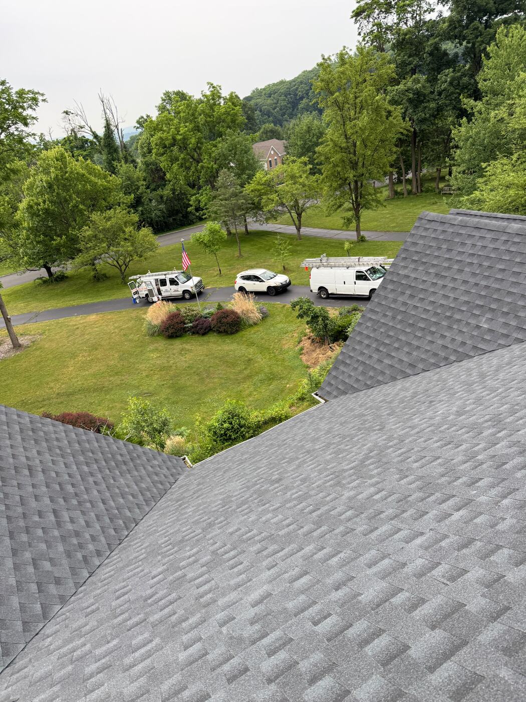 Aerial view over the completed hip roof toward the driveway and crew vehicles