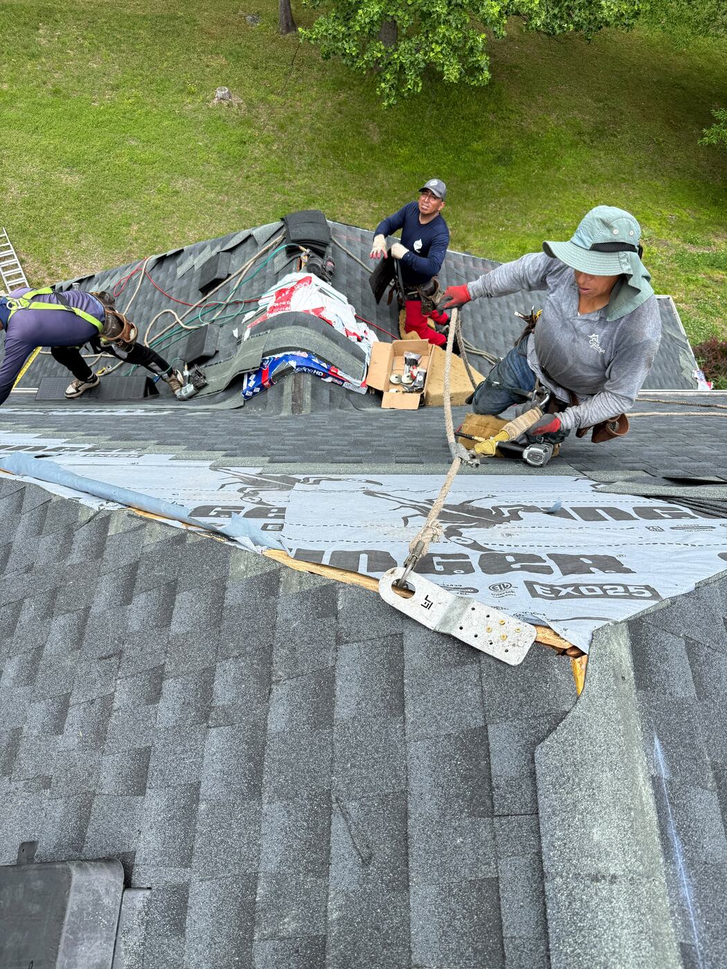 Roofing crew working in safety harnesses tied to a roof anchor while installing shingles